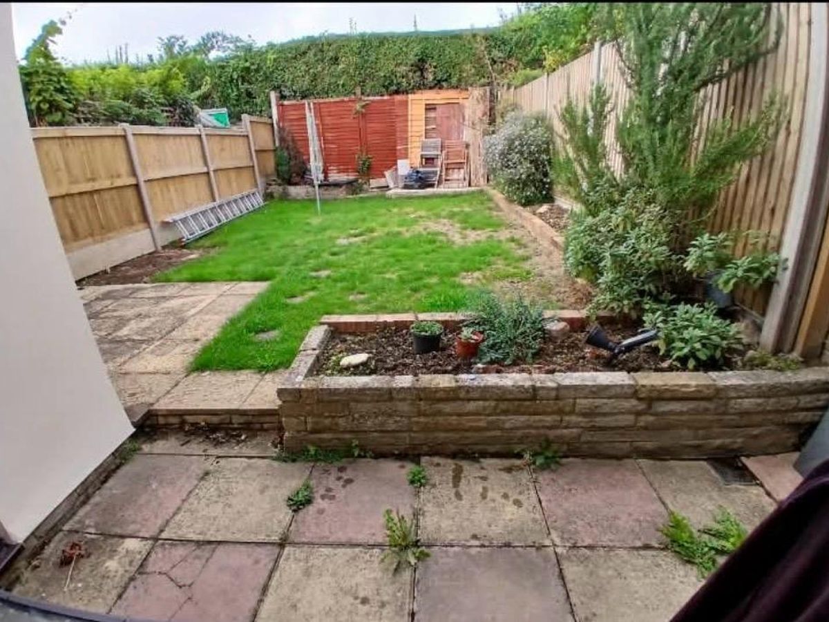 A tired Hoo garden before work started, with worn paving, a patchy lawn, an old raised planter bed and a weathered rear fence
