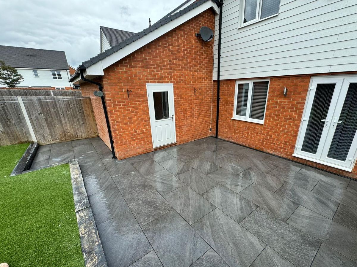 Dark grey porcelain paving laid as a terrace beside artificial grass and a brick house