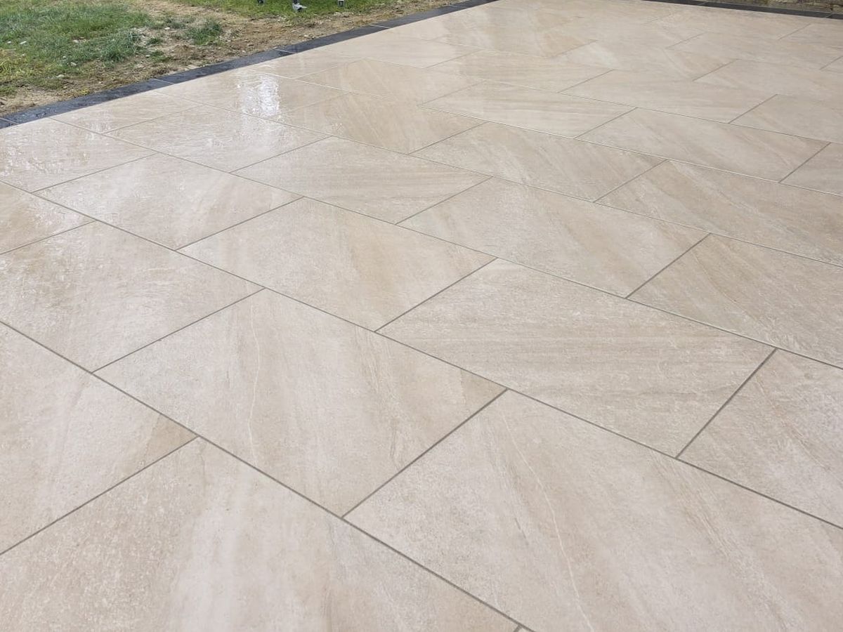 Large-format cream porcelain paving with a dark border course and channel drainage