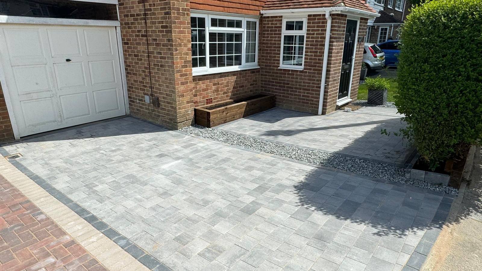 New grey block paving driveway with a charcoal border course, gravel margin and timber planter