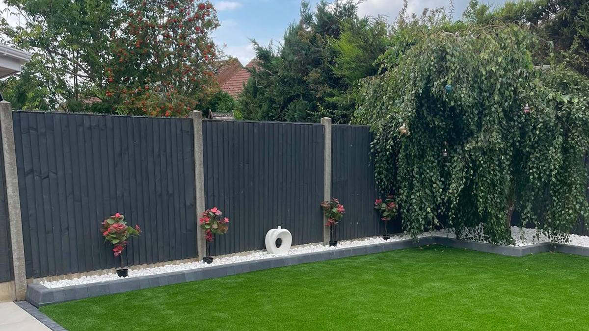 Closeboard fencing with concrete posts above a white gravel border and artificial lawn