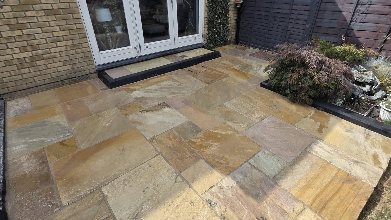 Indian sandstone patio paving laid in mixed tones beside a brick house with bi-fold doors