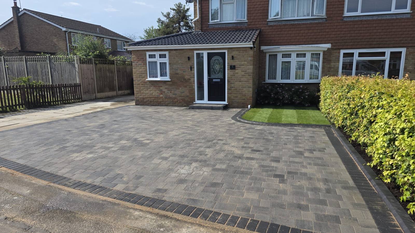 A completed grey block paving driveway with a curved border and new lawn