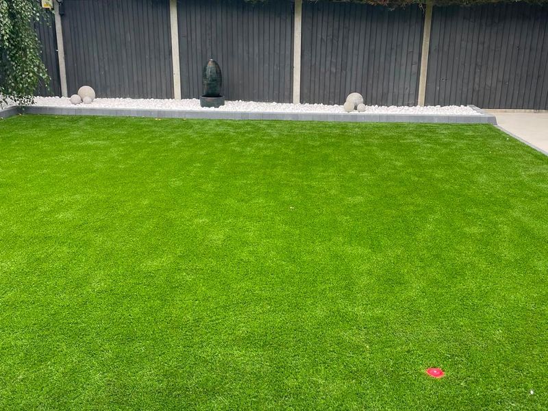 An artificial lawn laid to a planted gravel border and timber fencing