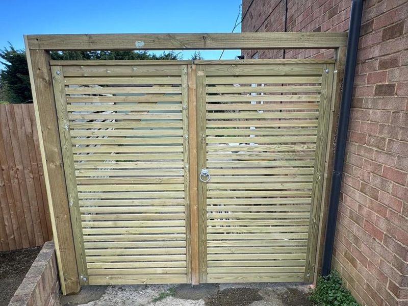 A slatted timber garden gate hung between a brick wall and a closeboard fence