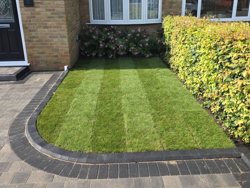 A new turf lawn edged with a curved charcoal block paving border